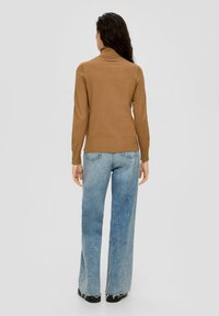 Bruine coltrui gecombineerd met lichtblauwe, wijde jeans. De outfit heeft een gladde textuur en een getailleerde stijl.