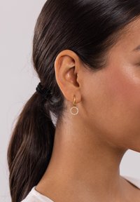 Goldene Creolen mit einem kreisförmigen Design, verziert mit kleinen klaren Steinen, die eine glatte Textur und einen glänzenden Finish zeigen.