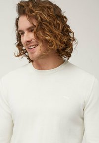 Maglione bianco a maniche lunghe con scollatura rotonda. Presenta un logo discreto sul petto e un tessuto morbido e texture.