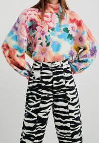 Jersey floral multicolor con cuello alto y corte holgado, combinado con pantalones de cintura alta con rayas de cebra en blanco y negro.