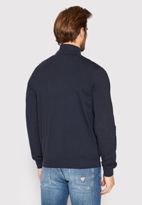 Felpa blu navy con colletto alto, maniche lunghe e polsini a coste. Tessuto liscio con vestibilità comoda. Dettaglio di cucitura visibile lungo le cuciture.