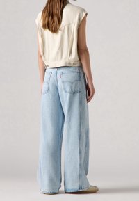 Breda ljusblå jeans i denim, kombinerade med en cropped, off-white ärmlös topp med en mjuk textur och minimal detaljering.