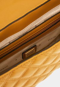 Gul quiltet håndtaskeindvendig med beige stofforing, lynlåslomme og guld Guess mærke syet indeni.