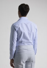Camisa de vestido a cuadros azules con mangas largas, puños abotonados y un cuello clásico, combinada con pantalones de traje gris claro.
