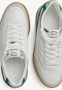 White retro sneakers with green accents, silver metallic details, suede texture, and a gum rubber sole. Features lace-up front and logo tag.