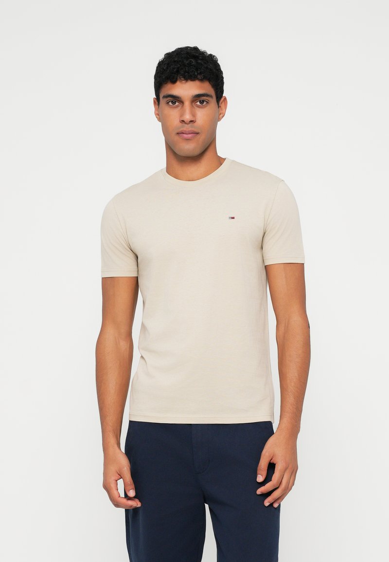 Μπεζ βαμβακερό t-shirt με στρογγυλή λαιμόκοψη και κοντά μανίκια. Διαθέτει ένα μικρό λογότυπο στο αριστερό στήθος. Φοριέται με ναυτικό μπλε παντελόνια.