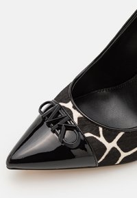 Escarpin à bout pointu en cuir verni noir avec une imprimé girafe texturé noir et blanc et un détail décoratif en métal noir avec le logo sur le devant.