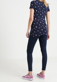 Camiseta navy con patrón de hojas blancas, de manga corta, combinada con jeans oscuros y zapatillas rosas. Diseño sencillo con ajuste relajado.