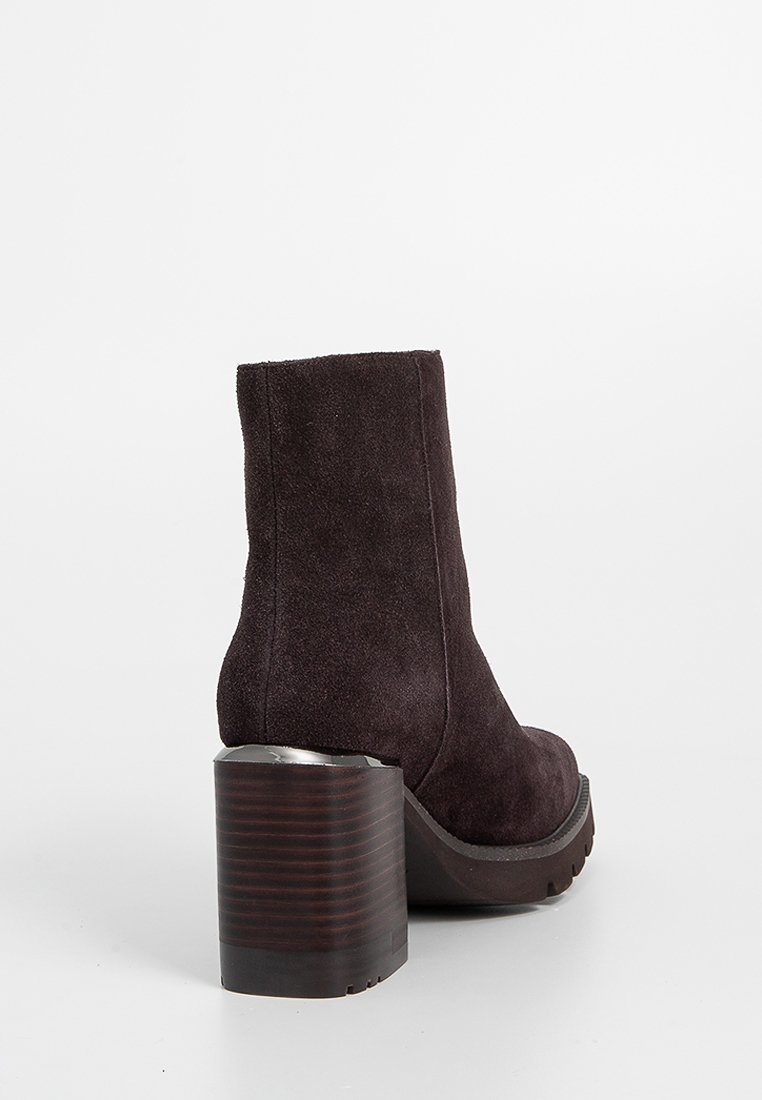 Botín de ante morado oscuro con un tacón de madera macizo y a rayas y una suela de goma suave. Presenta un diseño elegante y ajustado, sin herrajes visibles.