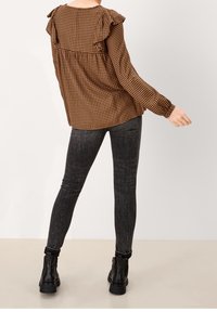 Blusa a quadri marrone con spalline arricciate, abbinata a jeans skinny grigi scuri e stivaletti neri. Look moderno e casual con texture contrastanti.