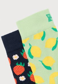 Ζεύγος πολύχρωμων καλτσών, μία πράσινη με κίτρινες λεμονιές και μία ναυτικό μπλε με κόκκινες φράουλες και λευκά λουλούδια.