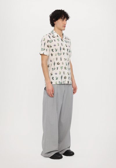 Camisa de manga corta con un fondo crema que presenta un estampado de cactus. Combinada con pantalones grises holgados y zapatos negros.