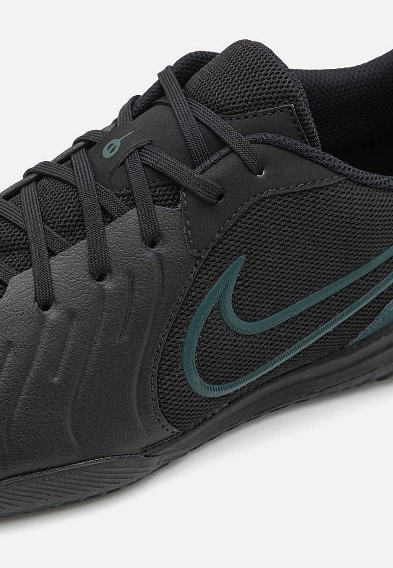 Baskets noires de sport avec une tige en cuir texturé et en maille, ornées d'un accent de logo vert foncé. Lacets étroitement tressés et semelle extérieure en caoutchouc.