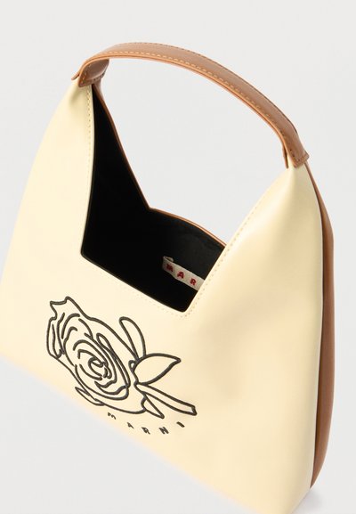 Τσάντα σε κρεμ και καφέ χρώμα με σχέδιο ραμμένο μαύρο τριαντάφυλλο και μία πάνω λαβή, μερικώς ανοιχτή που δείχνει το μαύρο εσωτερικό.