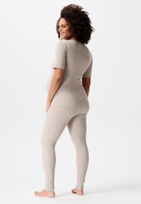Beige, enganliegendes Loungewear-Set aus weichem, dehnbarem Material. Das kurzärmlige Oberteil und die langen Hosen haben eine glatte Textur und dezente Nähte.