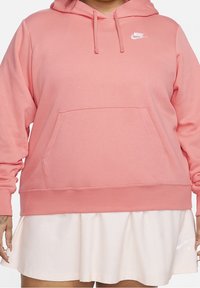 Rosa Nike-hoodie med en framficka, dragsko i huvan och vit logotyp. Tyget verkar mjukt med en slät struktur.