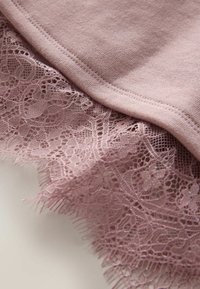 Pehmea mauve kangas, millel on detailne pitsäär, kus on lillemustrid ja geomeetrilised kujundid ääres.