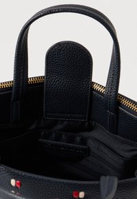 Geantă tote din piele texturată neagră cu fermoar auriu, manere superioare și un buzunar cu accente roșii și crem în interior.