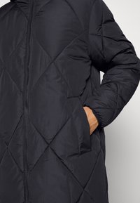 Veste matelassée noire avec zip à l'avant, motif en losanges, poches latérales et poignets élastiques pour le confort et la chaleur.