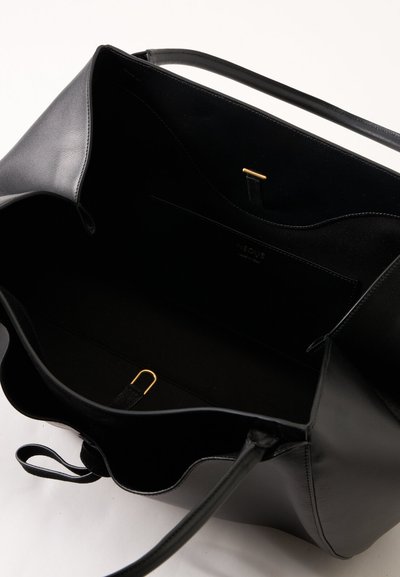 Sac cabas en cuir noir ouvert avec des anses fines, montrant un intérieur spacieux avec une petite poche intérieure et des détails en métal doré.