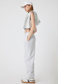 Grijze cropped zip hoodie met een capuchon, gecombineerd met grijze trainingsbroek. Accessoires zijn een witte pet en witte sneakers met zwarte accenten.