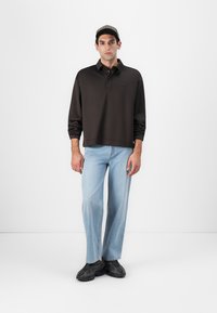 Polo à manches longues noir, jean droit bleu clair et baskets noires. Design simple avec un col et une coupe décontractée.