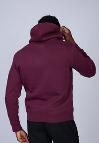 Hoodie bordeaux en tissu doux, avec une capuche à cordon, des manches longues et des poignets et un ourlet côtelés. Design simple et épuré.