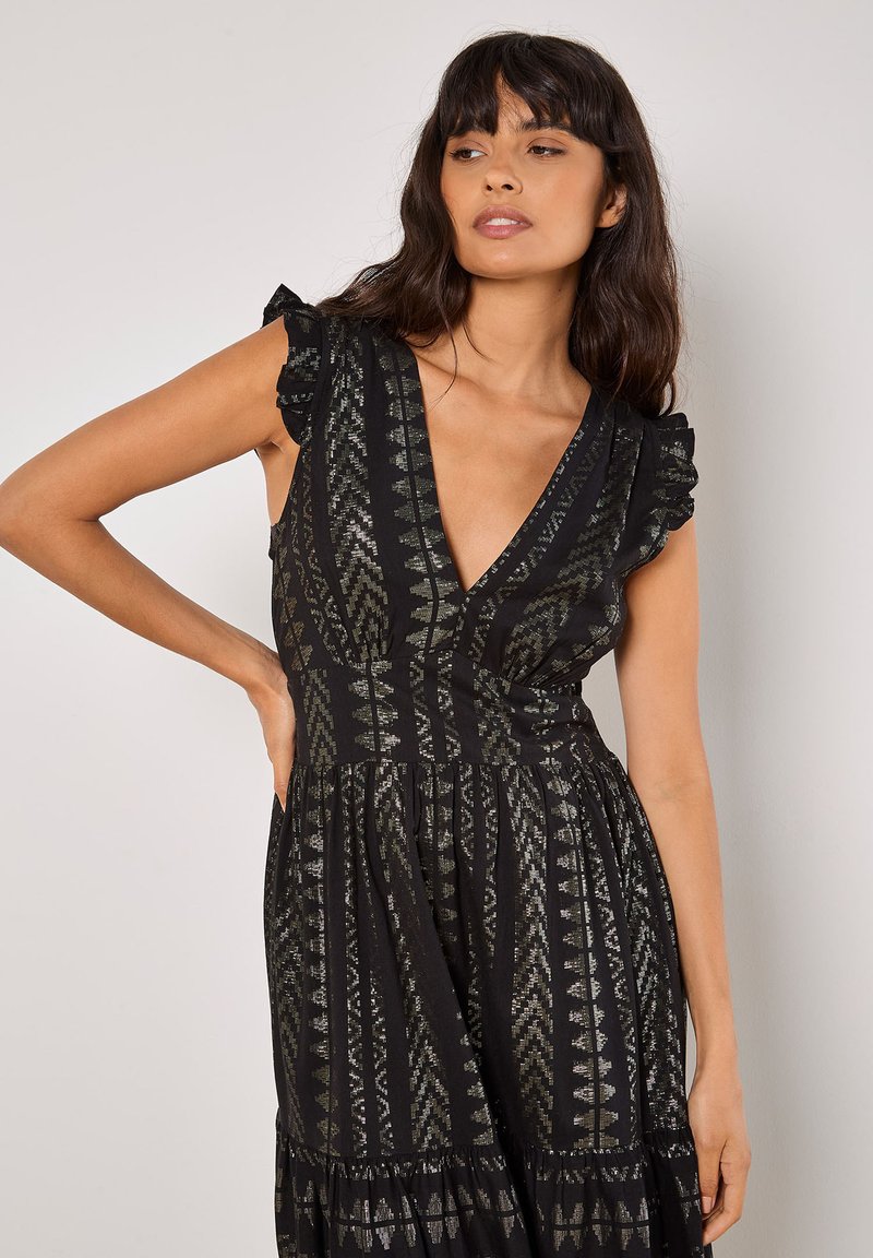 Robe noire avec un décolleté en V profond, des manches à volants et des détails en argent complexes ; jupe fluide avec un ourlet froncé.