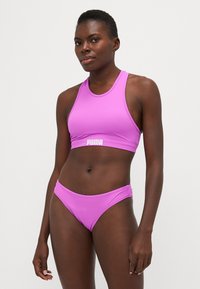 Rožinės sportinės bikini komplektas, kuriame yra berankovė viršutinė dalis su apvaliu iškirpimu ir atitinkamos žemos juosmens kelnaitės, pagamintos iš lygaus, tamprios medžiagos.