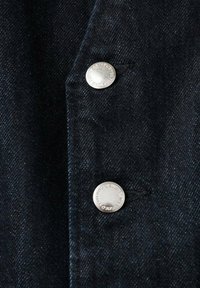 Tela de mezclilla oscura con una textura sutil que presenta dos botones de metal plateado, colocados cerca uno del otro, en el lado izquierdo.