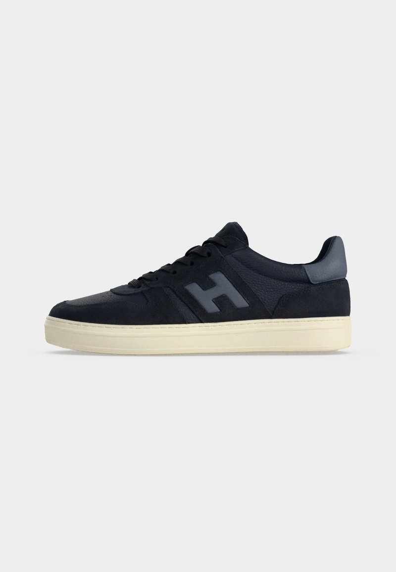 Black low-top sneaker with beige sole, lace-up front, and a large textured H logo on the side.