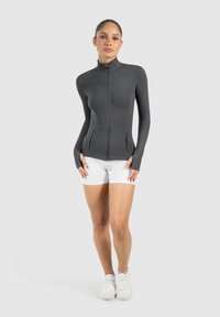 Zwarte zip-up jas met een hoge kraag, slim fit ontwerp en zijzakken. Gemaakt in combinatie met witte shorts en sportieve schoenen. Glad textuur.