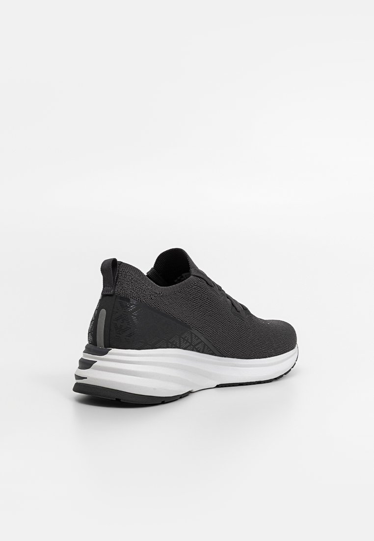Schwarzer Sportschuh mit einem strukturierten Strickobermaterial, konischer Silhouette und weißer, gepolsterter Sohle. Besitzt ein dezentes geometrisches Muster an der Ferse.