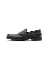 Mocasines de cuero negro con textura suave, puntera redondeada, acentos cosidos y un tacón bajo en bloque. Diseño minimalista sin adornos.