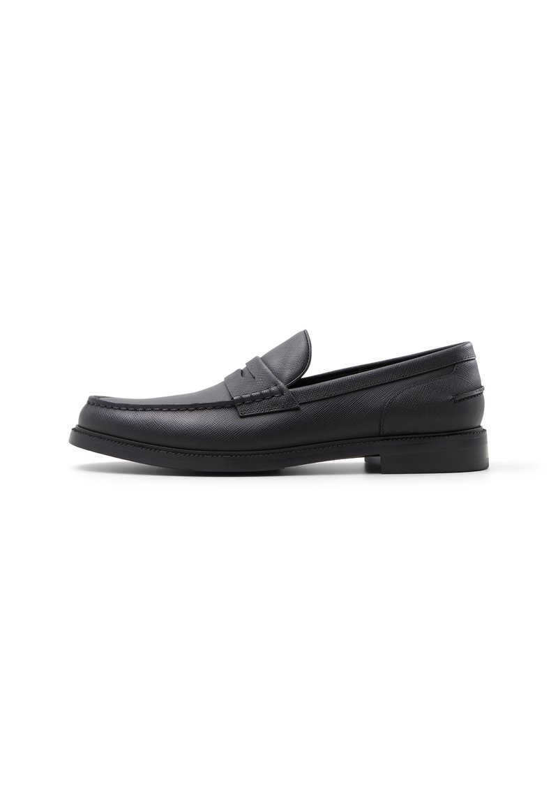 Mocasines de cuero negro con textura suave, puntera redondeada, acentos cosidos y un tacón bajo en bloque. Diseño minimalista sin adornos.