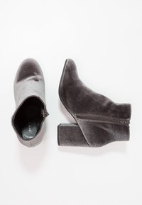 Botas de tobillo de terciopelo gris con un grueso tacón de bloque, punta afilada y detalle de cremallera lateral. Textura suave con un acabado ligeramente brillante.