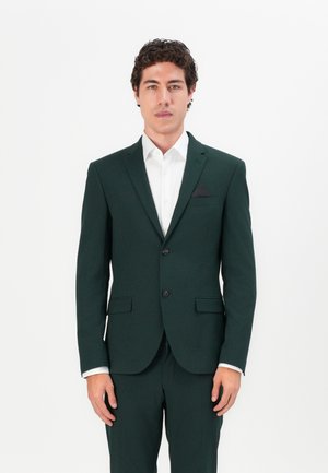Dunkelgrüner Anzug mit einreihiger Jacke, zwei Knöpfen, Revers und Brusttasche. Darunter ein weißes Hemd mit glatter Textur.
