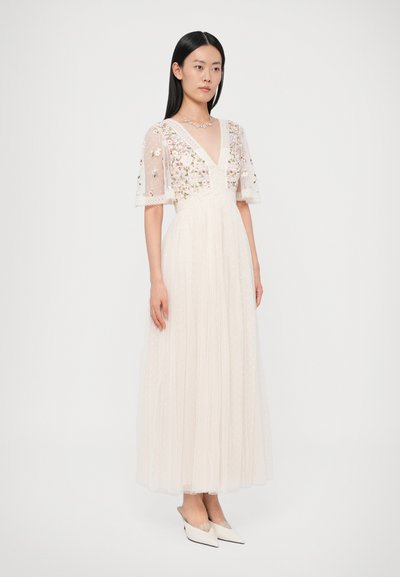 Μακρύ ελεφαντόδοντο φόρεμα με λουλουδάτη κέντημα, διαφανείς μανσέτες και ντεκολτέ σε σχήμα V. Κατασκευασμένο από ελαφρύ ύφασμα με πολλαπλές στρώσεις και υφασμένη φούστα.