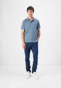 Svetlo modra kratkotrajna polo majica z teksturiranim vzorcem, v kombinaciji z mornarsko modrimi slim-fit hlačami in belimi supergami. Preprost dizajn, sproščen videz.