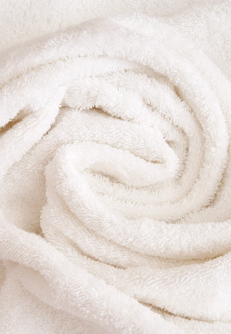 Asciugamano bianco e soffice arrotolato a spirale. Tessuto morbido con tessuto a loop, colorazione uniforme e senza schemi o hardware visibili.