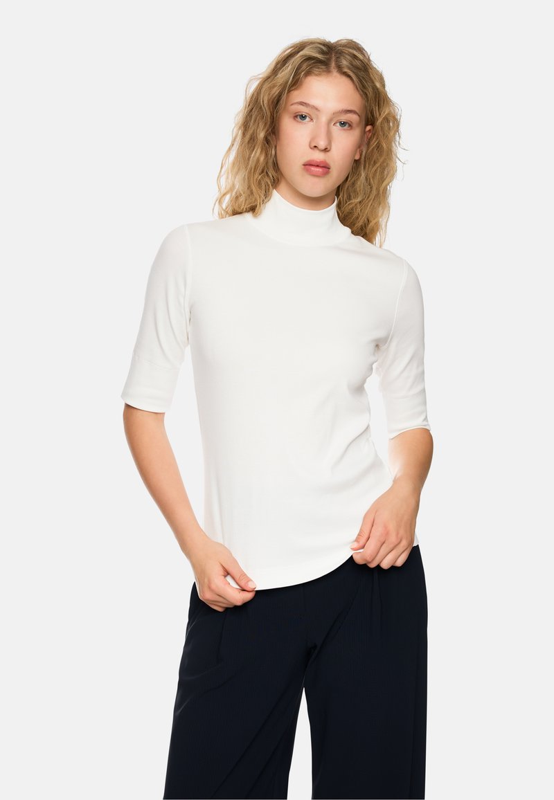 Weißes, tailliertes Turtleneck-Oberteil mit kurzen Ärmeln, glatter Textur und elegantem Design, kombiniert mit dunklen, weit geschnittenen Hosen.