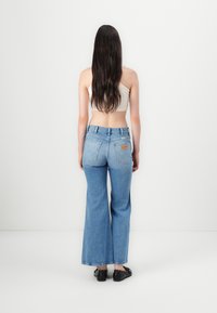 Jeans azzurri chiari a vita alta con gambe larghe, tasche posteriori ben visibili e etichetta in pelle. Indossati con un crop top aderente color crema.