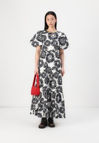 Lång svartvitt blommönstrad klänning med puffärmar, kombinerad med en röd handväska och bruna stövletter, mot en neutral bakgrund.