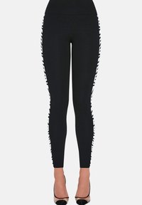 Czarne dopasowane legginsy z białymi paskami z napisem po zewnętrznych stronach, noszone z przezroczystymi szpilkami z czarnymi czubkami.