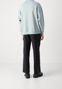 Ljusblå oversized sweatshirt med rundad krage, i kombination med svarta raka byxor och svarta skor med spännen.