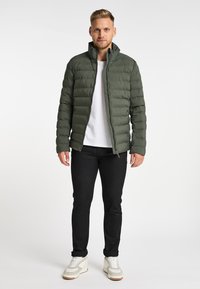 Groene gewatteerde jas met een staande kraag, voorzien van een ritssluiting. Draag over een wit T-shirt, gecombineerd met zwarte jeans en sneakers.