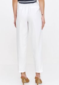 Białe, proste spodnie z elastycznym paskiem, o gładkiej teksturze. Noszone z cielistymi szpilkami.