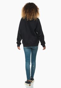 Svart sweatshirt med avslappnad passform, ribbad mudd och nederkant, kombinerad med ljusblå skinny jeans och svarta sneakers med vita sulor.