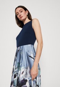 Sleeveless dress with a navy top and a floral patterned blue skirt, featuring a fitted bodice and flowing lower section.