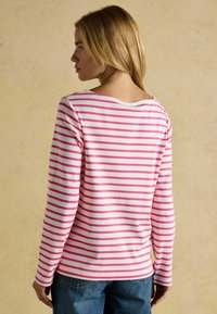 Dlhý rukáv v bielej farbe s ružovými horizontálnymi pruhmi, s širokým výstrihom a mäkkou tkaninou, skombinovaný s modrými džínsami.